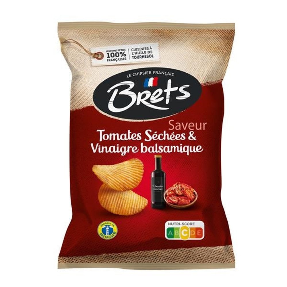 Un paquet rouge et brun sur fond blanc avec 2 chips, un bol de tomates séchés et une bouteille noire