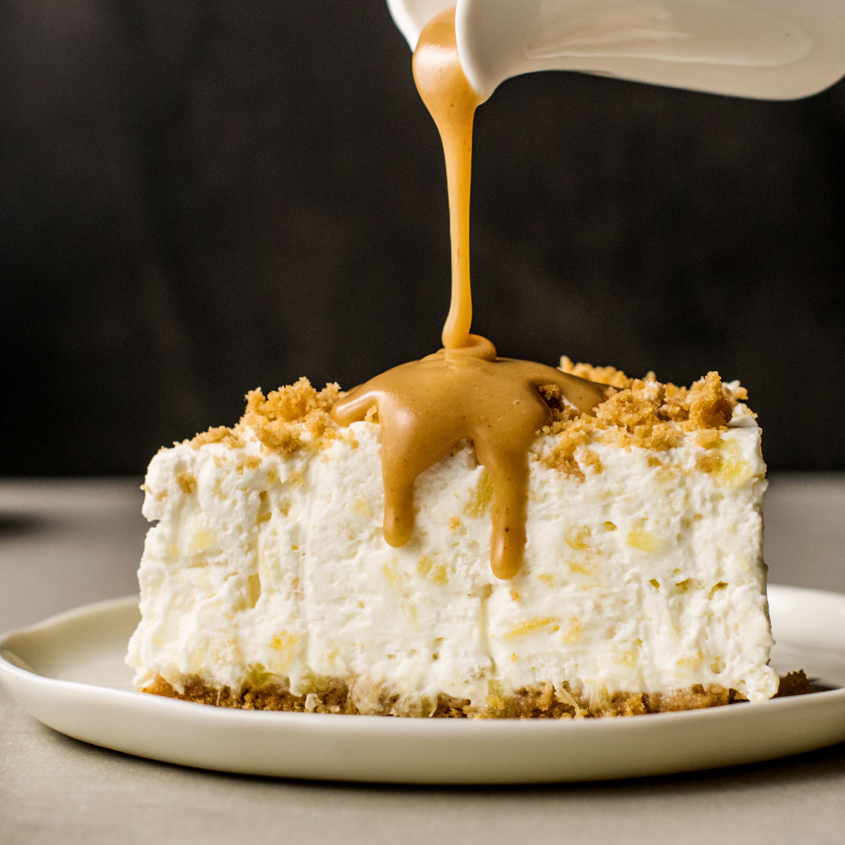 Un gâteau à la crème blanche avec un liquide brun qui coule dessus, le tout dans une assiette blanche avec un fond noir